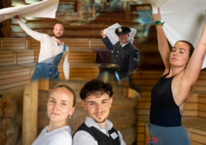 Fünf Personen in einer Sauna, zwei heben Handtücher über den Kopf, drei schauen in die Kamera, einer trägt eine Uniform mit Mütze